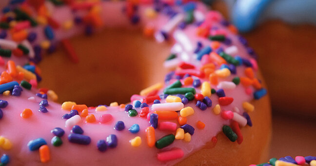 Donut mit rosa Guss und bunten Streuseln