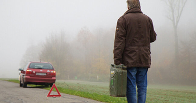 stehengebliebenes Auto am Straßenrand und Mann mit Kanister